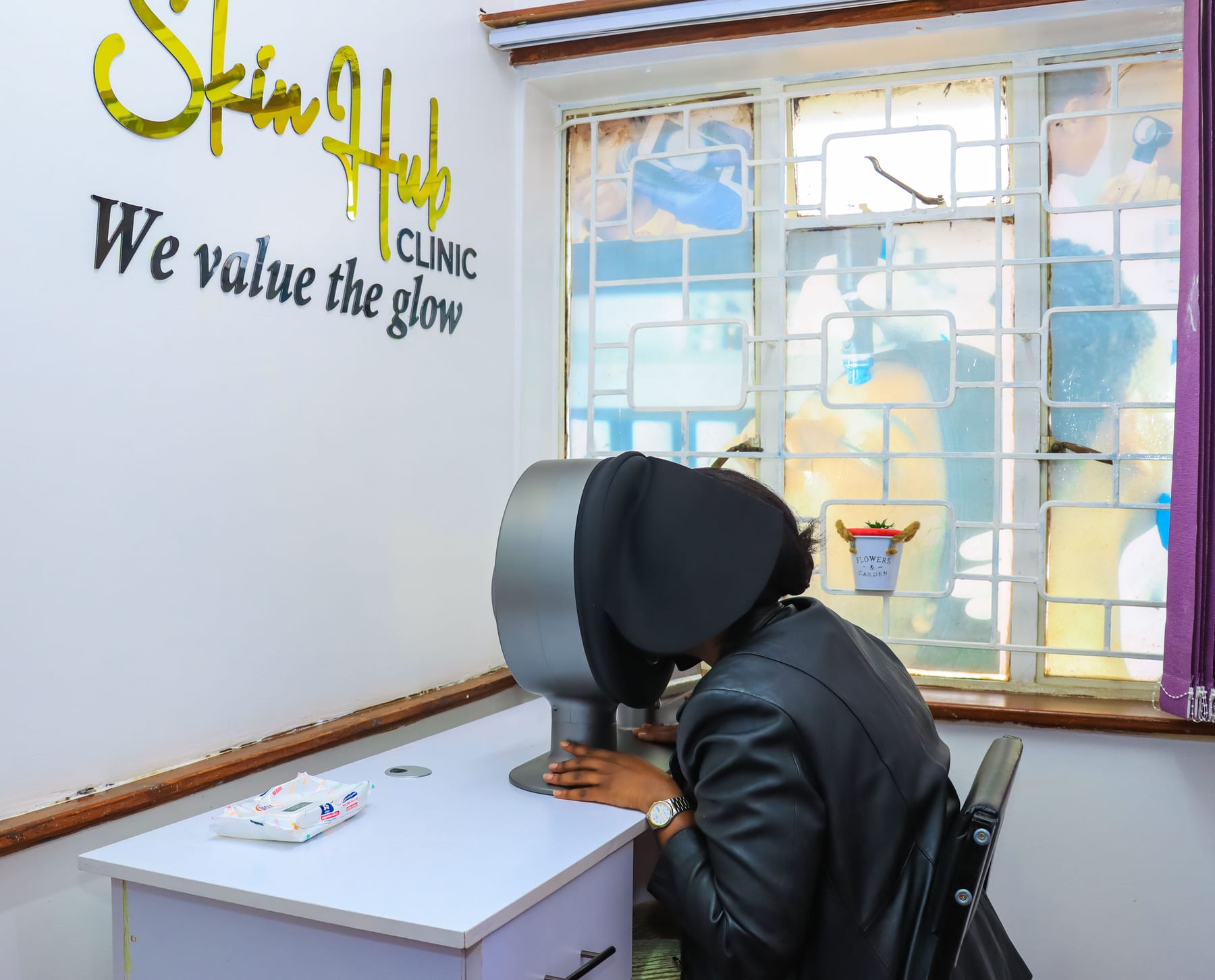 A patient seated at the digital skin analysis scanner in the Skinhub Clinic consultation room